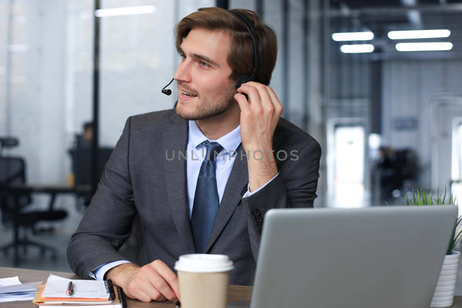 Cheerful young support phone male operator in headset, at workplace while using laptop, help service and client consulting call center concept. by tsyhun