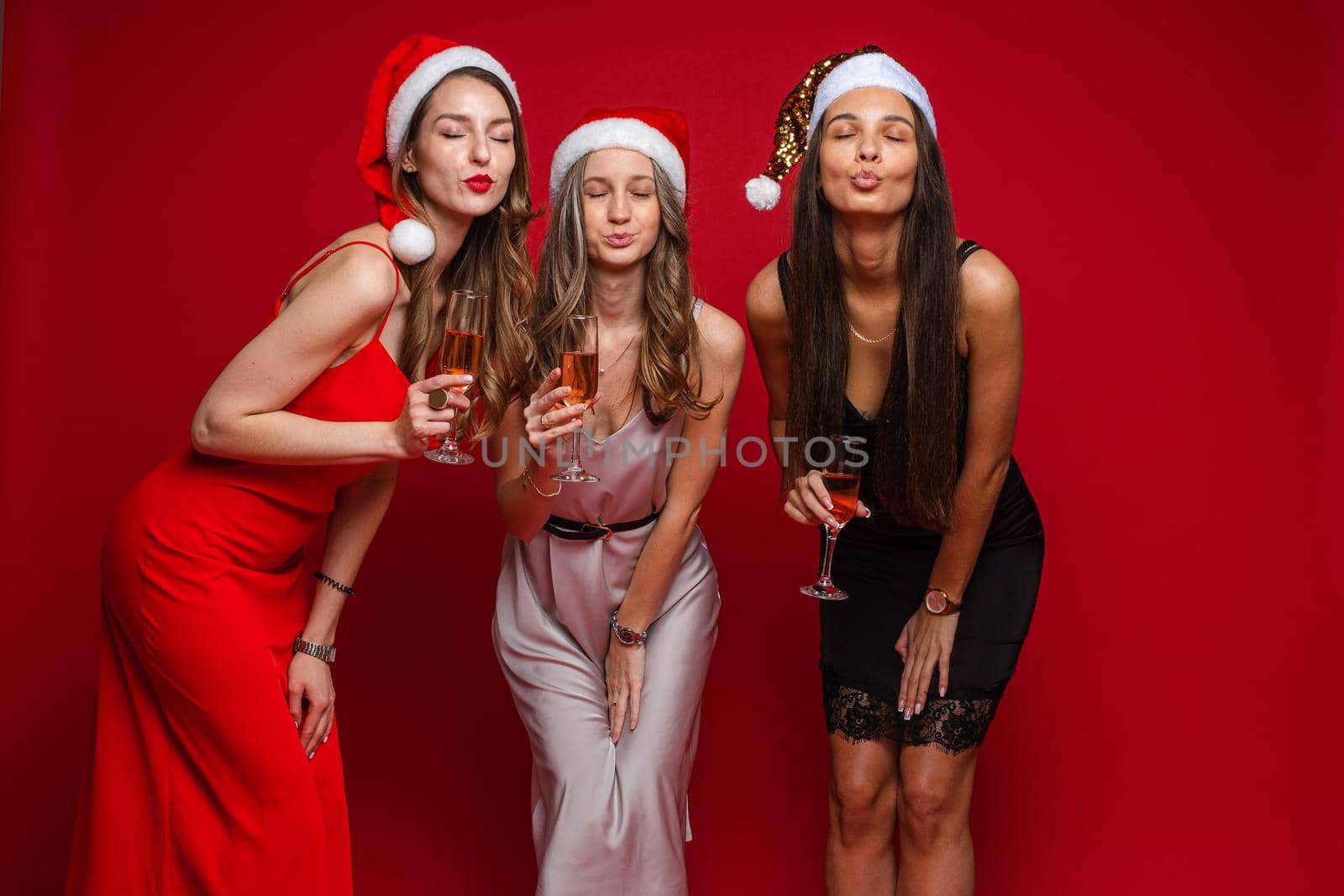 three cheerful female friends in beautiful dresses celebrate new year and rejoices together by StudioLucky