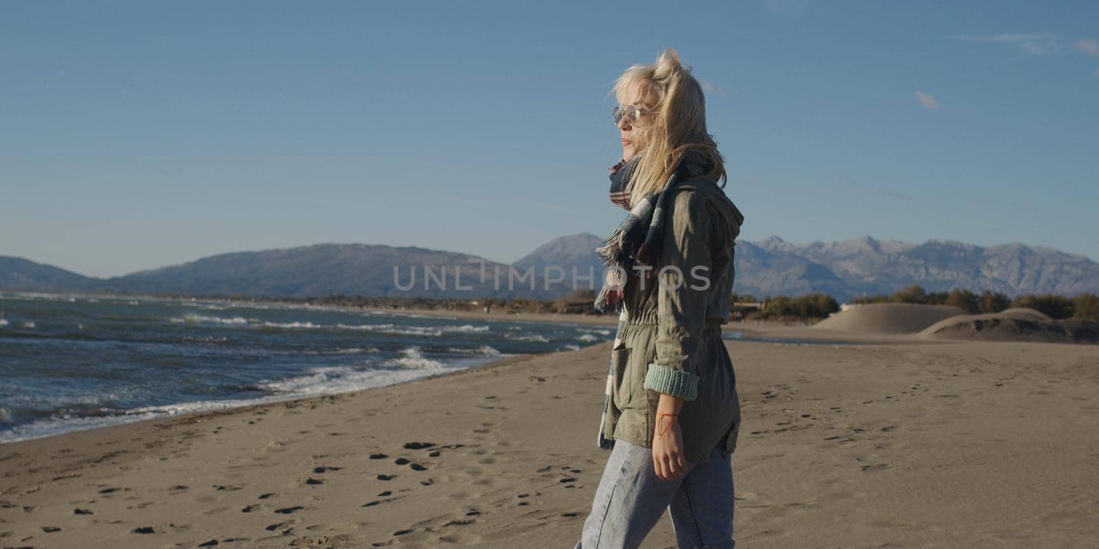 Young woman on the beach. The girl enjoying the warm autumn day. Portrait of beautiful girl near the water