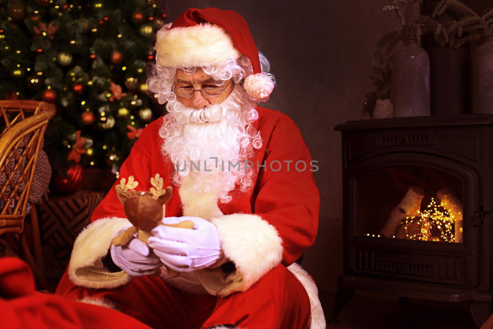 Portrait of happy Santa Claus sitting at his room at home near Christmas tree with toys