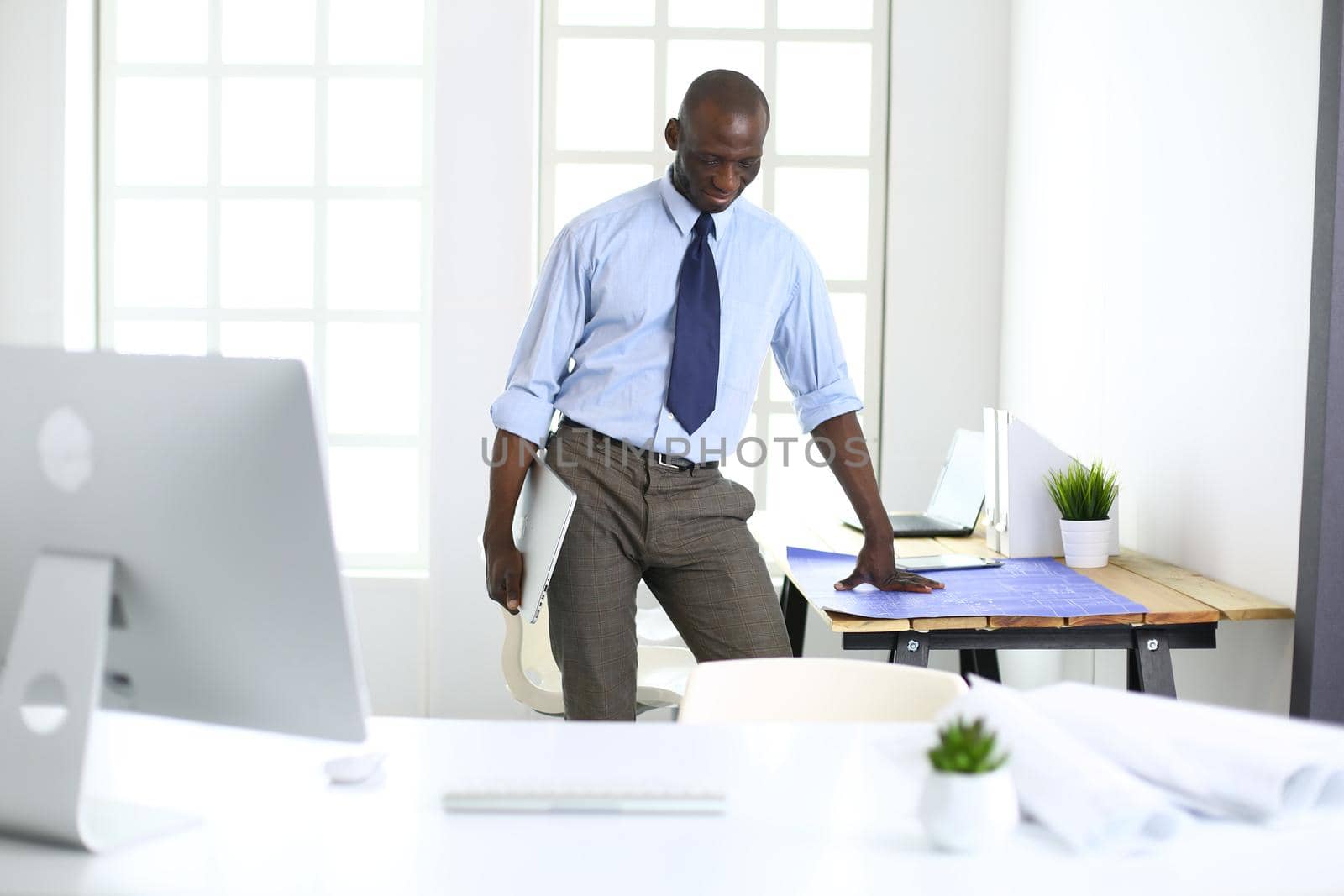 African american architect working with computer and blueprints in office.