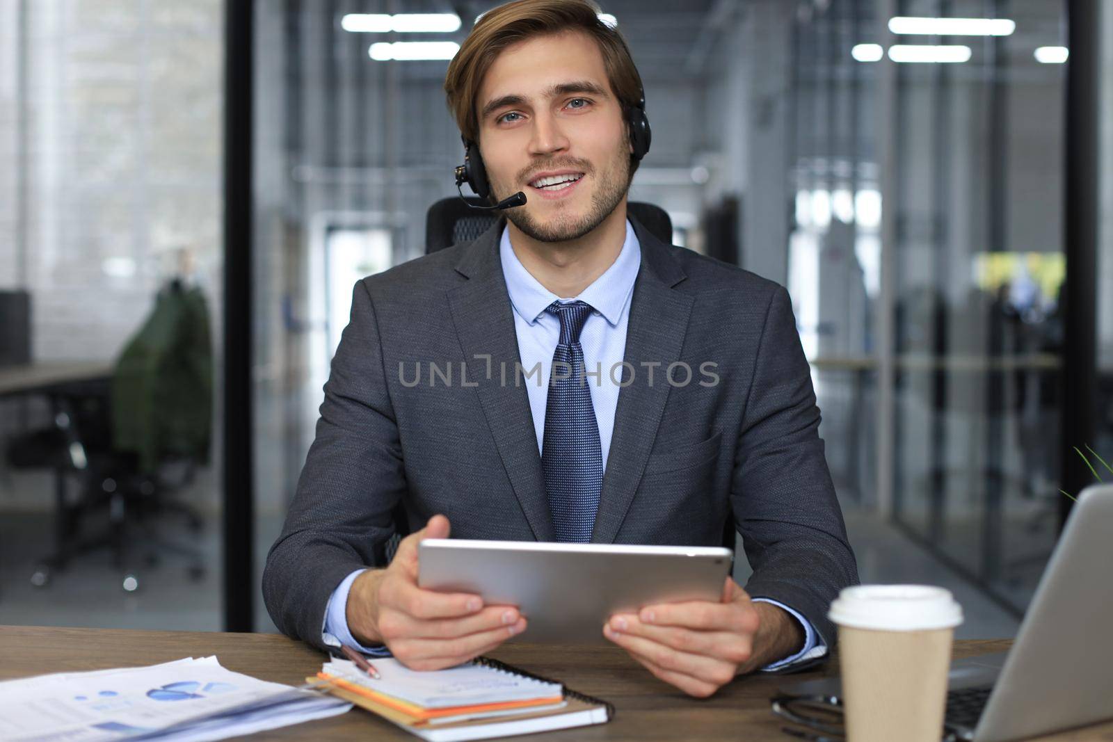 Cheerful young support phone male operator in headset, at workplace while using laptop, help service and client consulting call center concept.