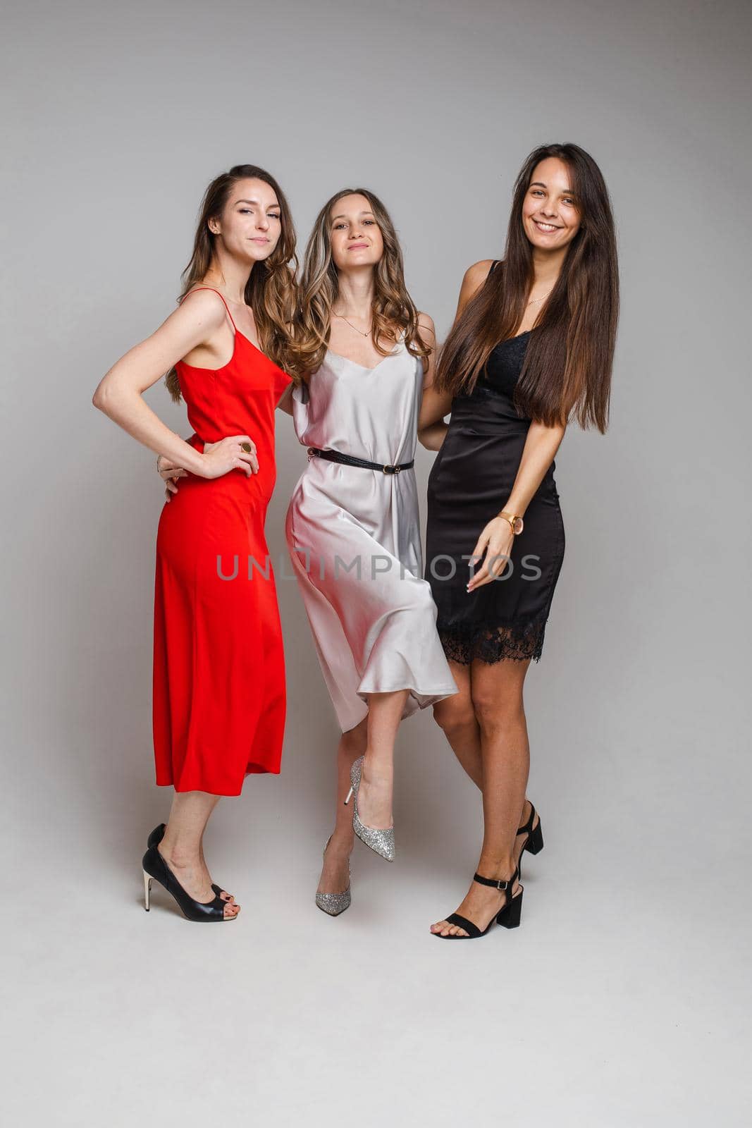 three cheerful female friends in beautiful dresses by StudioLucky