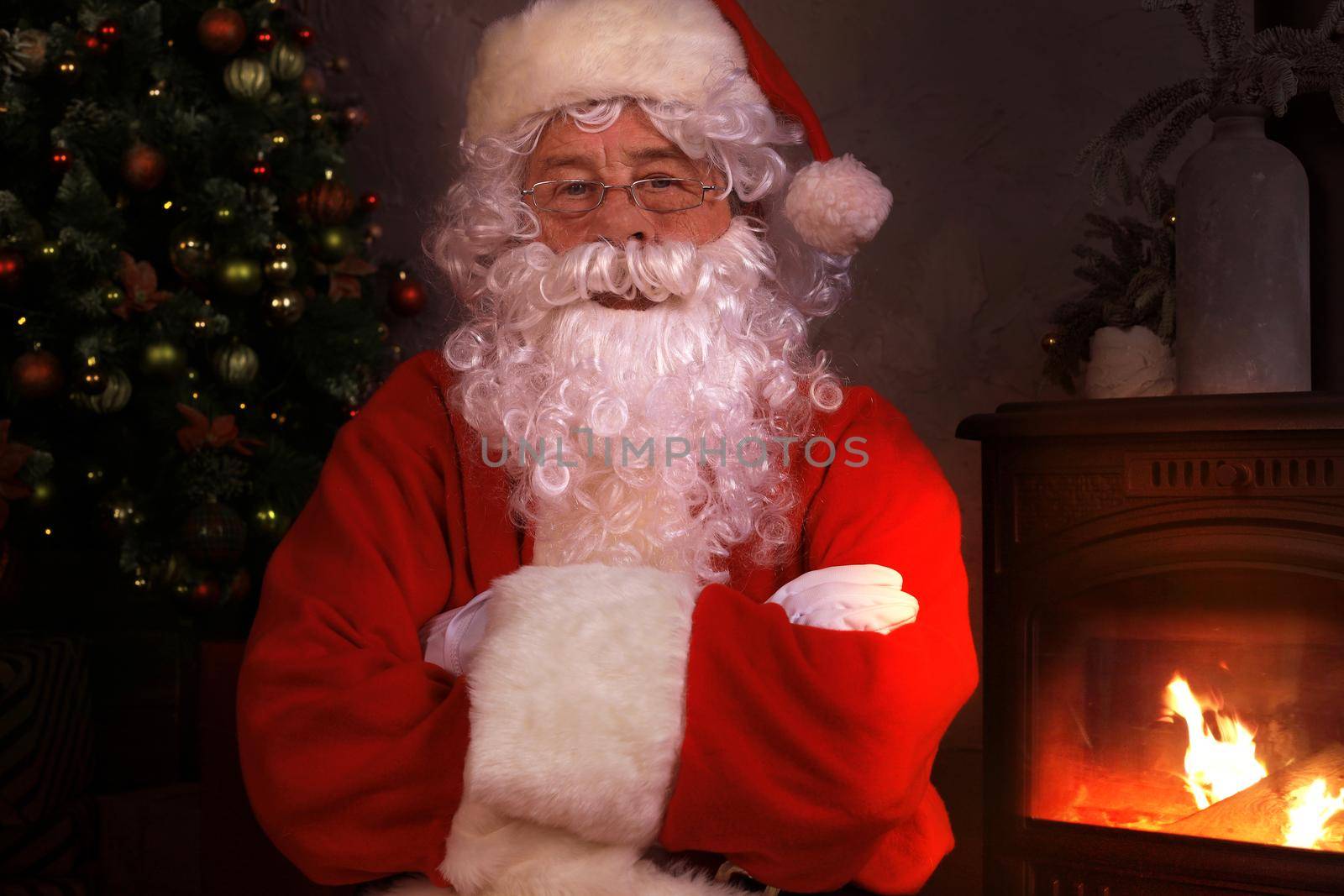 Traditional Santa Claus standing by the fireplace and Christmas tree in a room