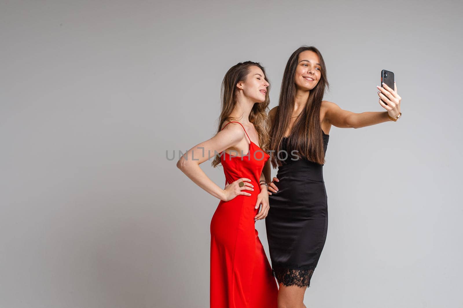 Smiling ladies in in silk dresses using mobile phone to take photo together by StudioLucky