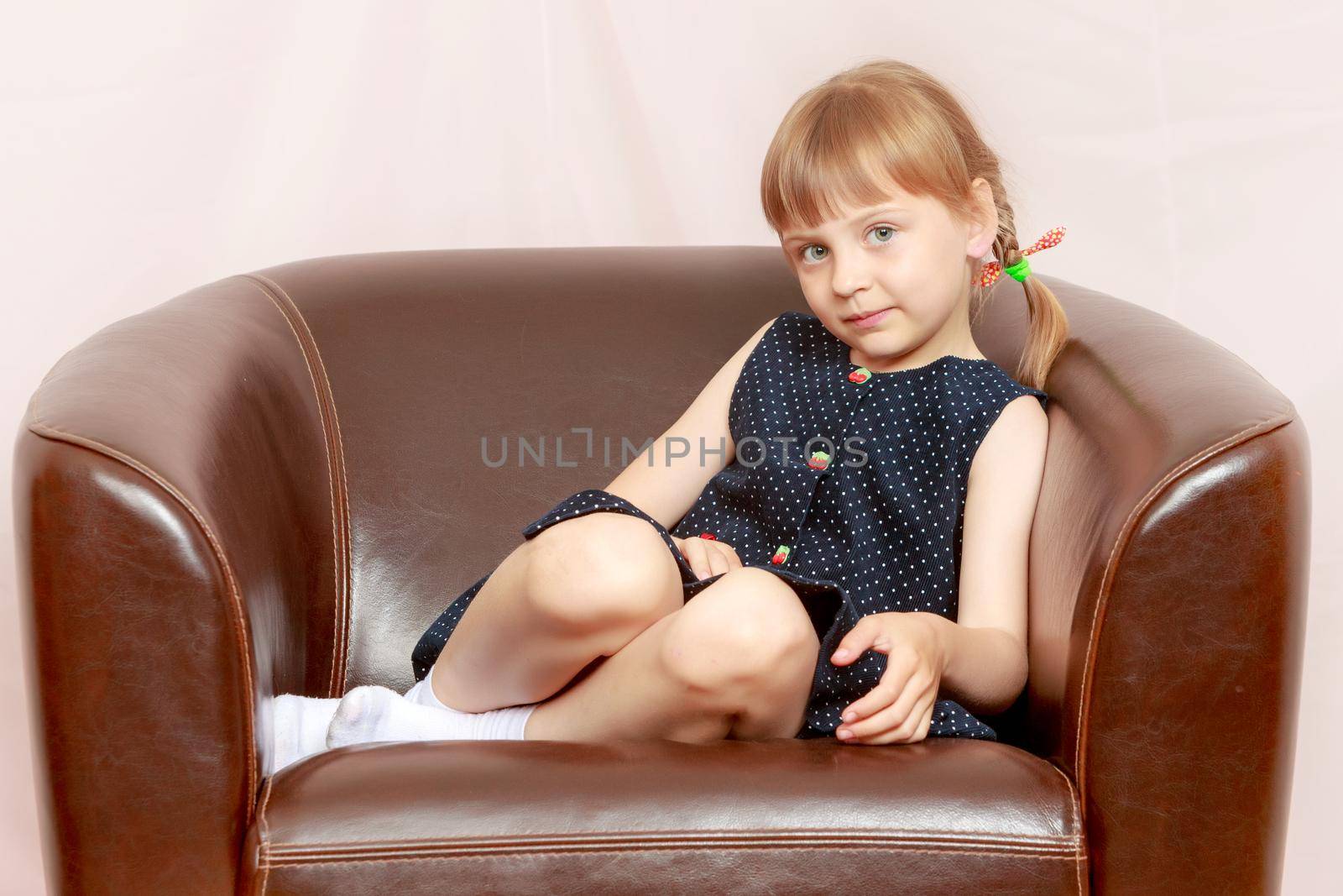A little girl is sitting on a leather chair. by kolesnikov_studio
