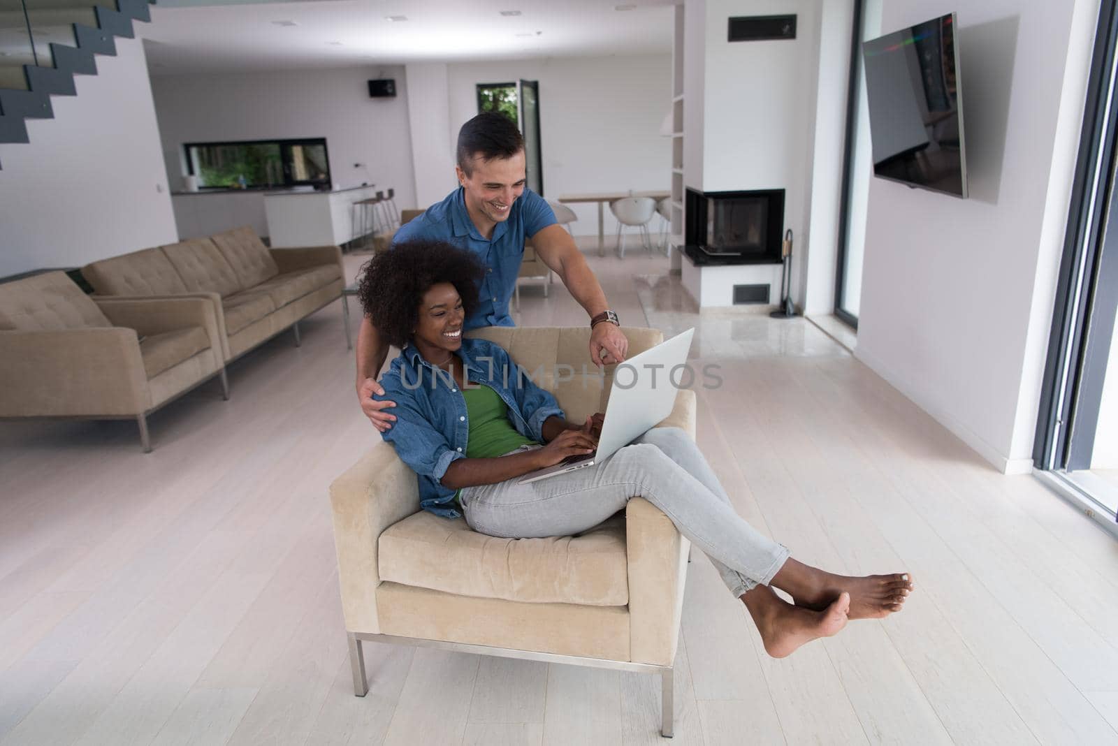 Young multiethnic couple sitting on an armchair in the luxury living room, using a laptop computer