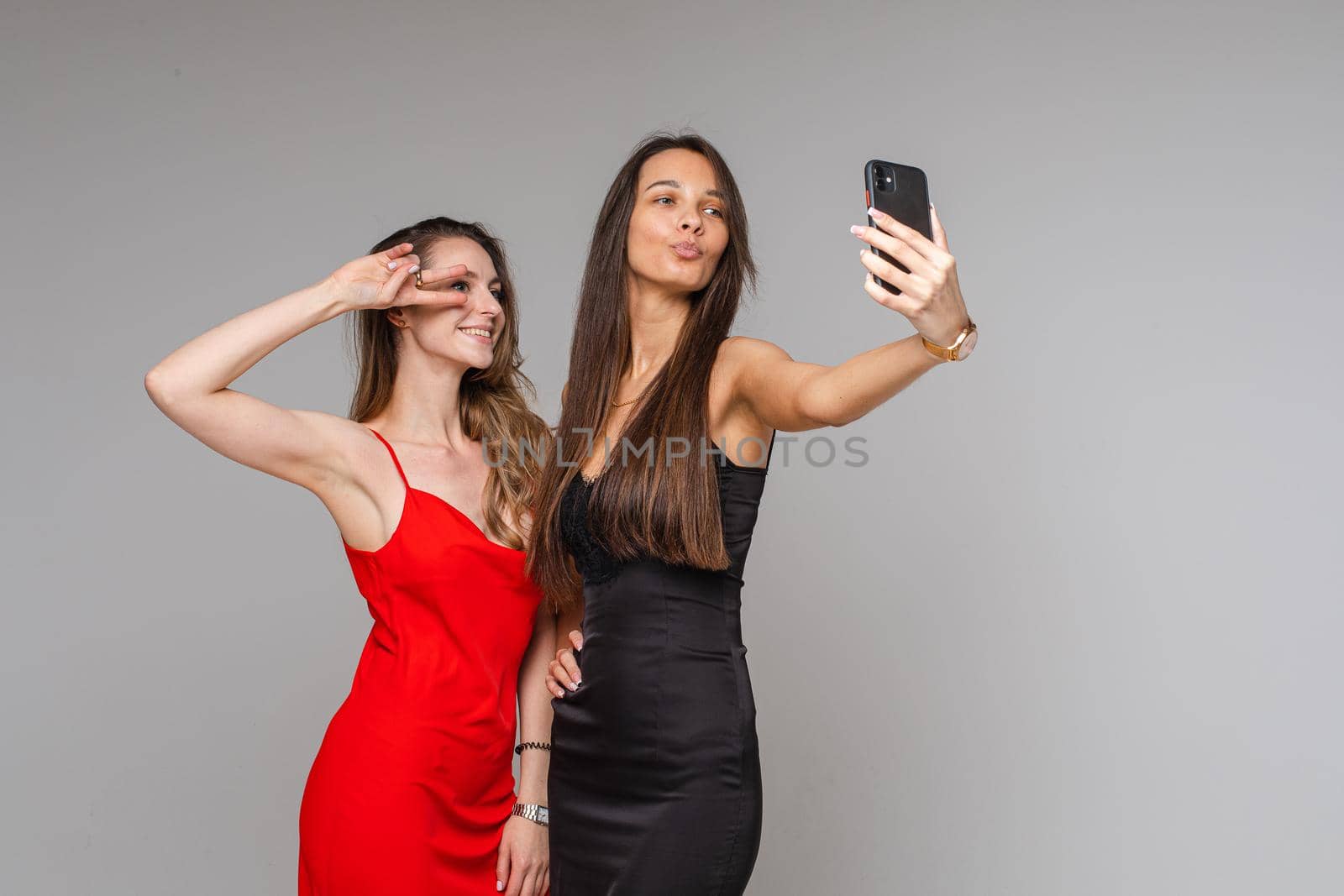 Pretty young girls bloggers wearing stylish dresses make selfie photography using phone posing on gray studio background. High quality photo