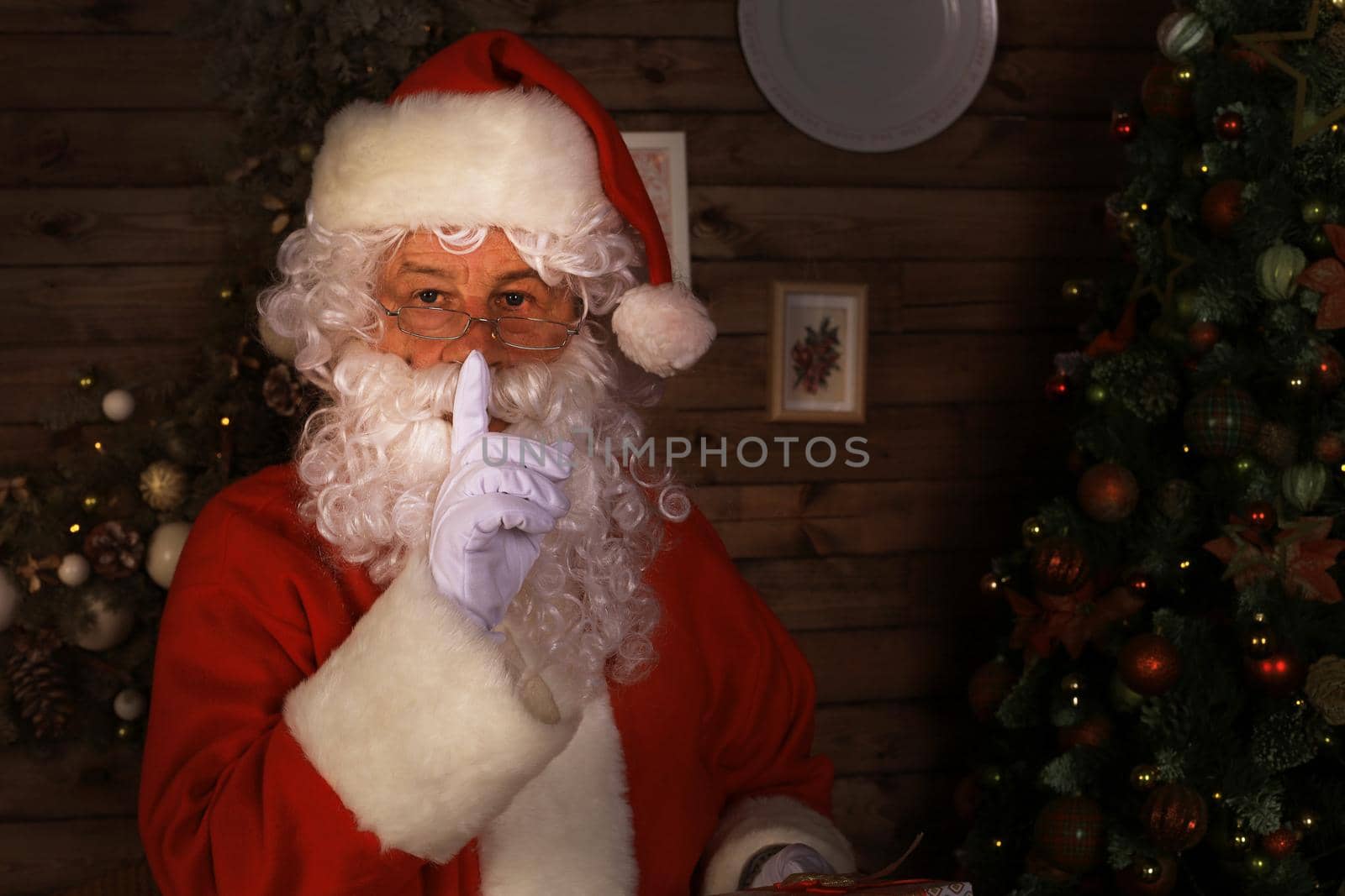 Portrait of Santa Claus keeping forefinger by his mouth and looking at camera