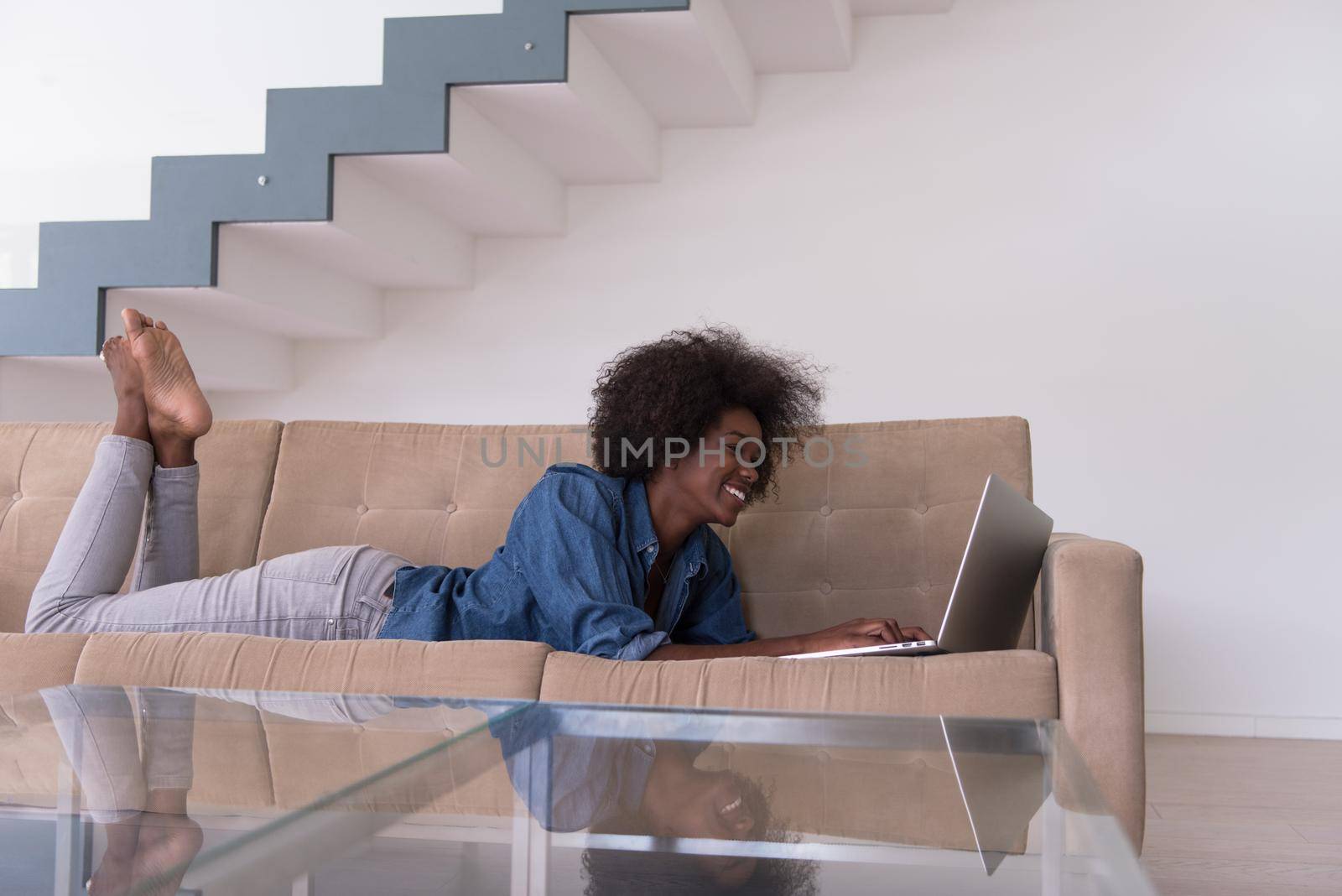 African American woman using laptop on sofa by dotshock