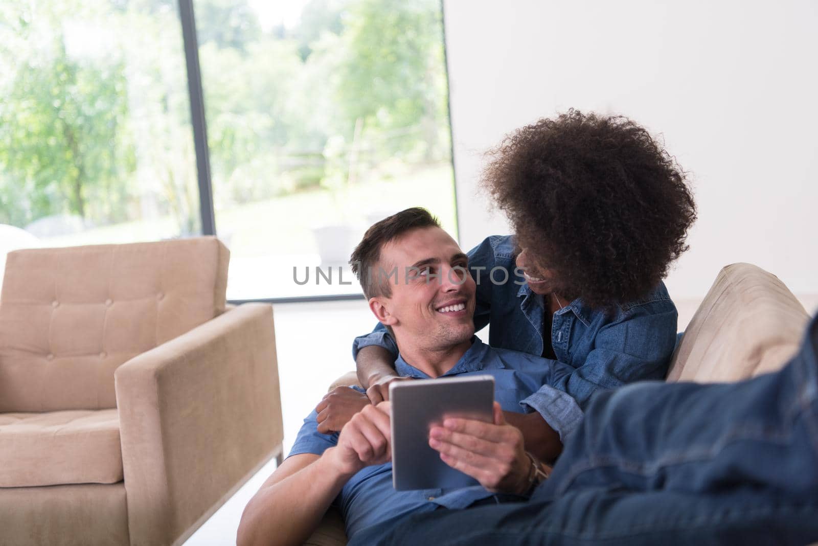 Young multiethnic couple relaxing at luxurious home with tablet computers reading in the living room on the sofa couch.