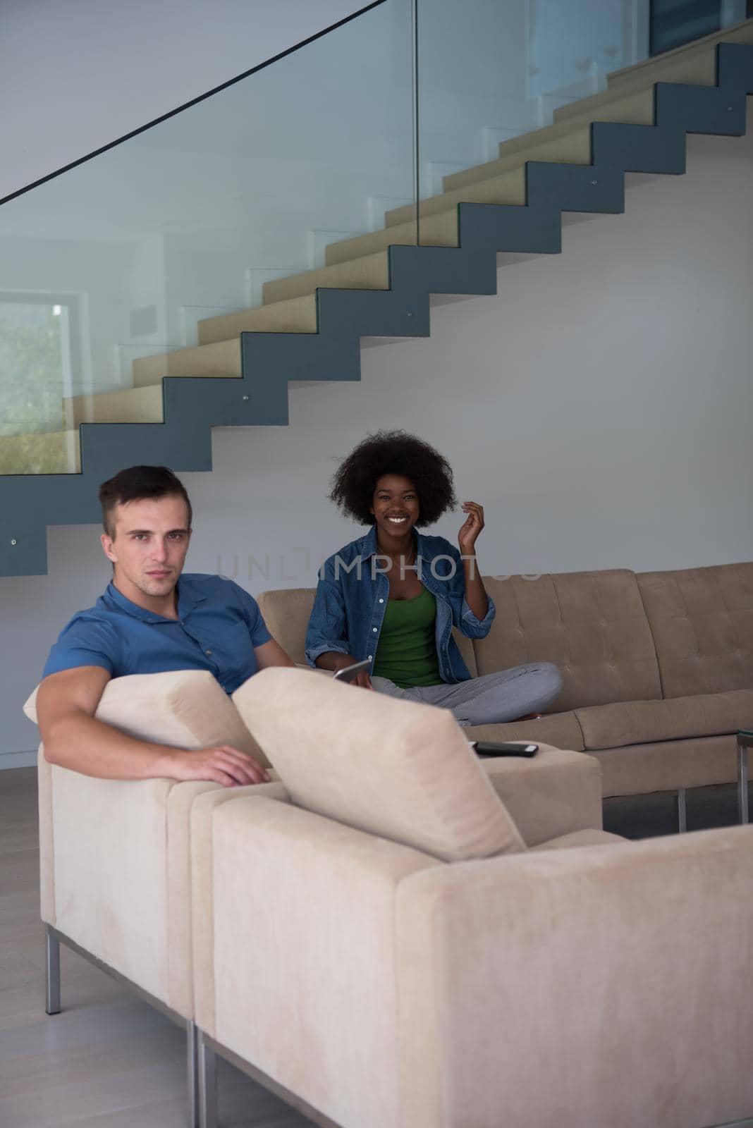 Young multiethnic couple relaxing at luxurious home with tablet computers reading in the living room on the sofa couch.