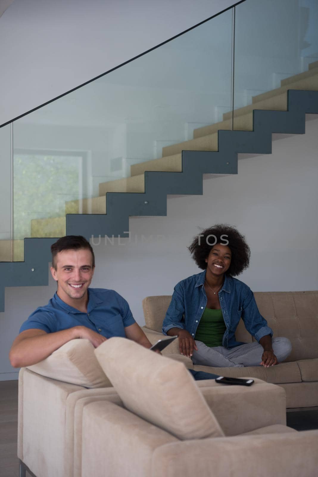 Young multiethnic couple relaxing at luxurious home with tablet computers reading in the living room on the sofa couch.