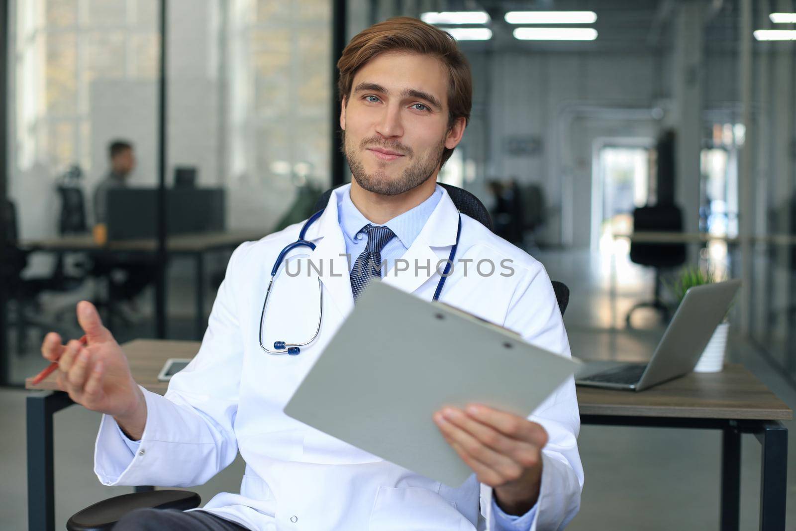 Smiling handsome male doctor talking at camera with patient