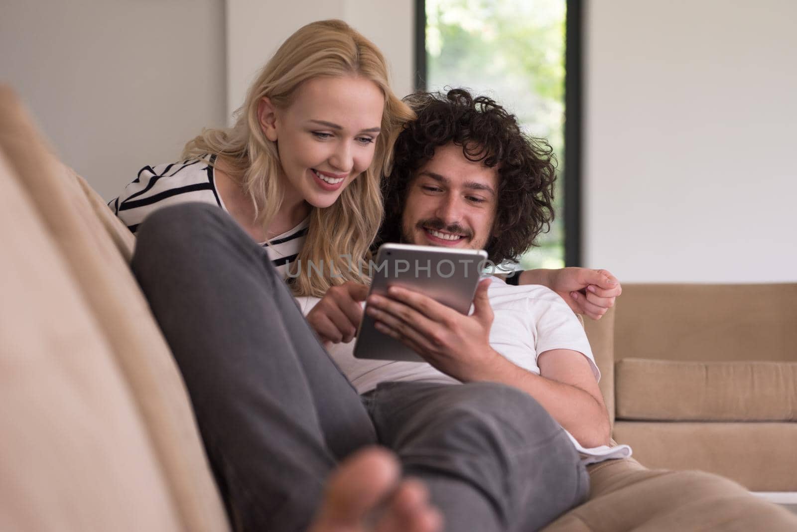 Young couple relaxing at luxurious home with tablet computers reading in the living room on the sofa couch.