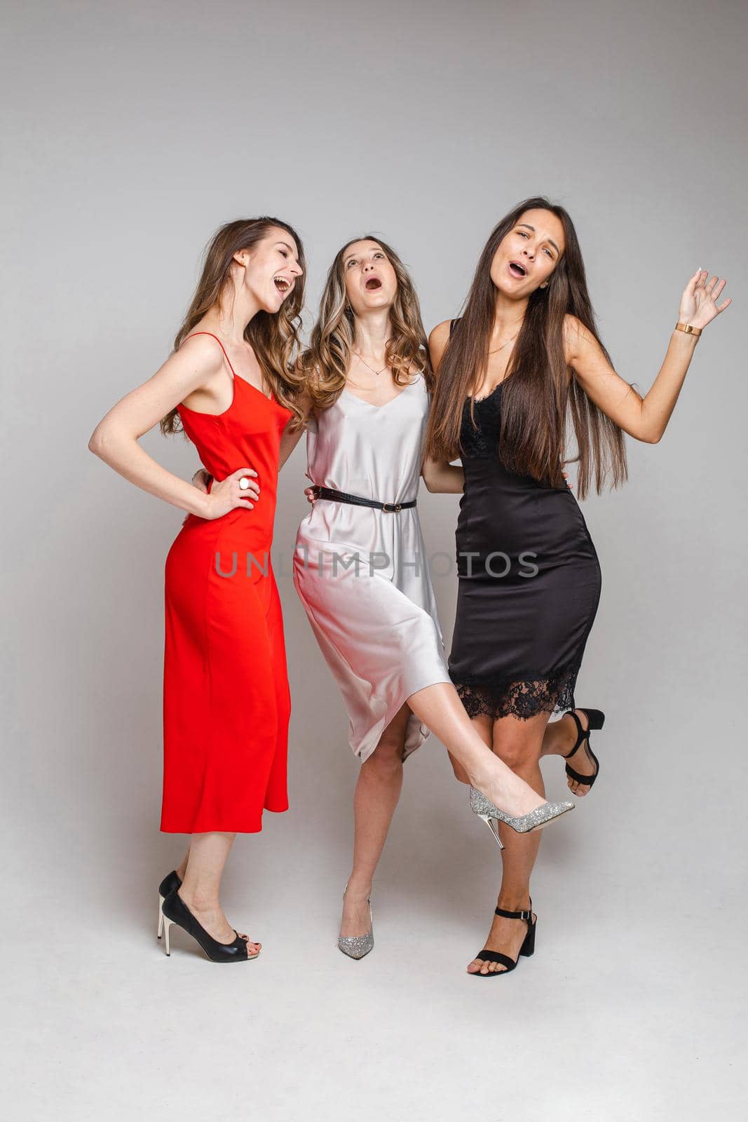 three cheerful female friends in beautiful dresses, isolated on white background