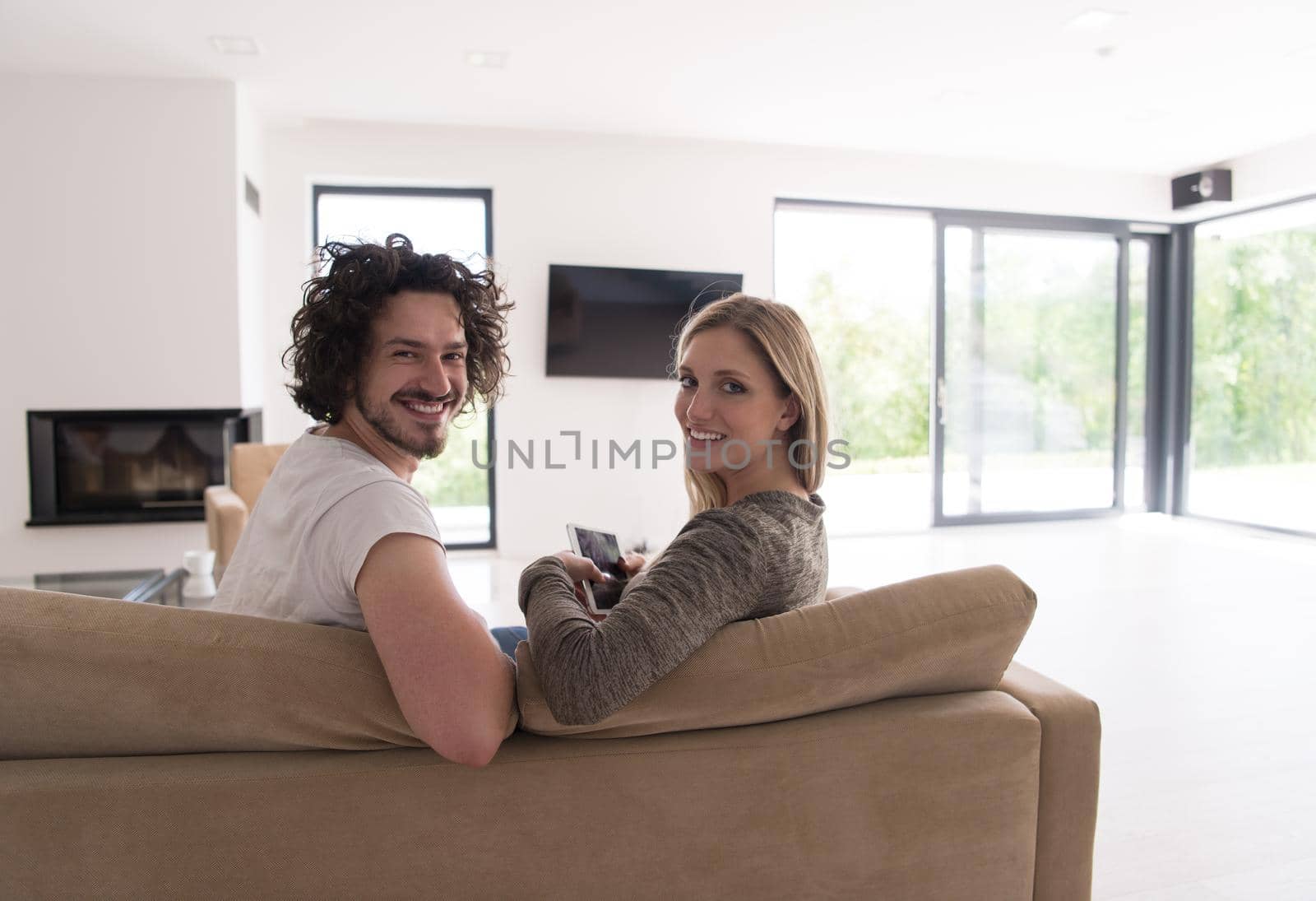 Rear view of couple watching television in living room their luxury home