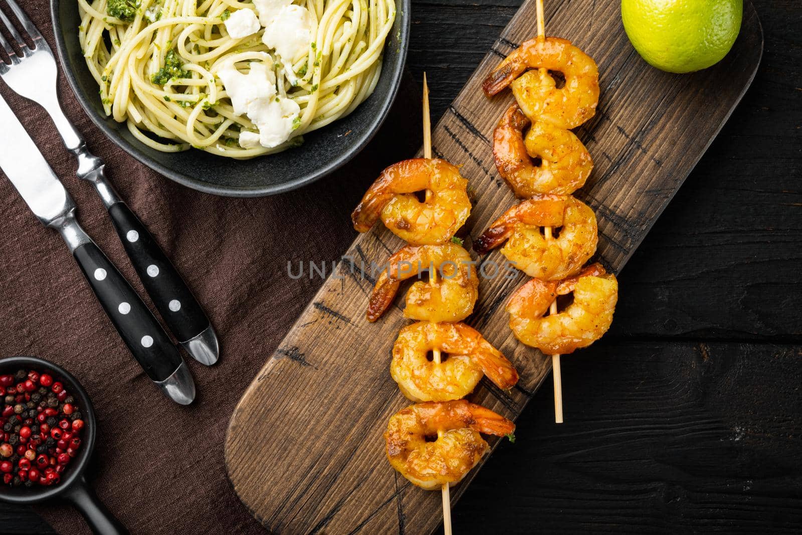 Italian pasta spaghetti with grilled shrimps, pesto sauce set, on black wooden table background, top view flat lay