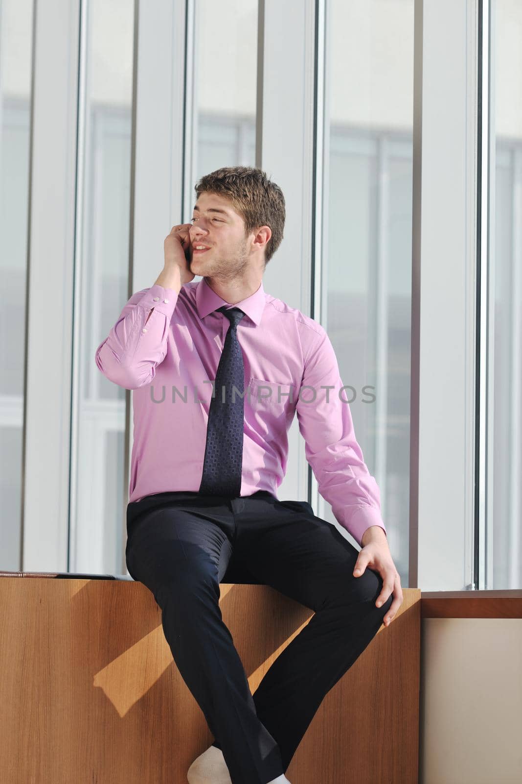 young business man talk by cellphone over bright window in big hall