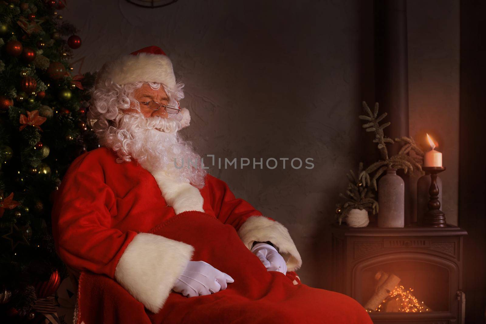 Santa Claus having a rest in a comfortable chair near the fireplace at home