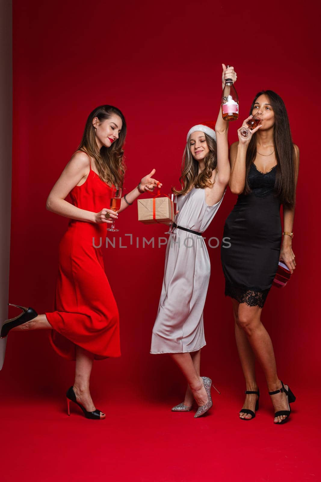 three cheerful female friends in beautiful dresses celebrate new year by StudioLucky
