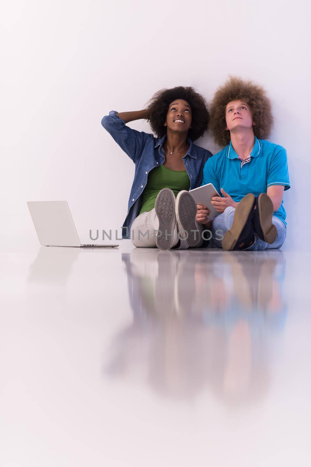 multiethnic couple sitting on the floor with a laptop and tablet by dotshock