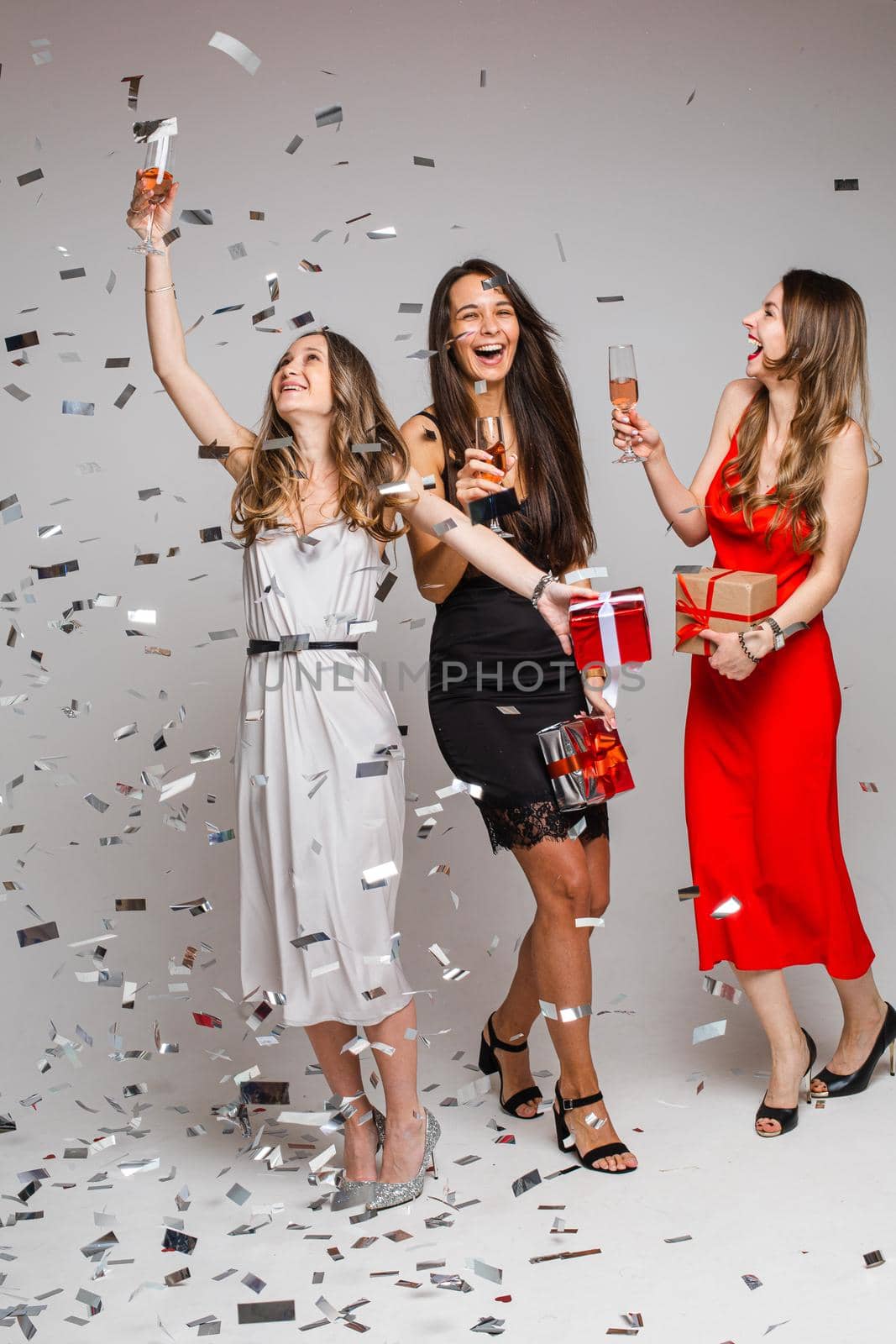 beautiful female friends in dresses with champagne and a lot of confetti around them, isolated on white background