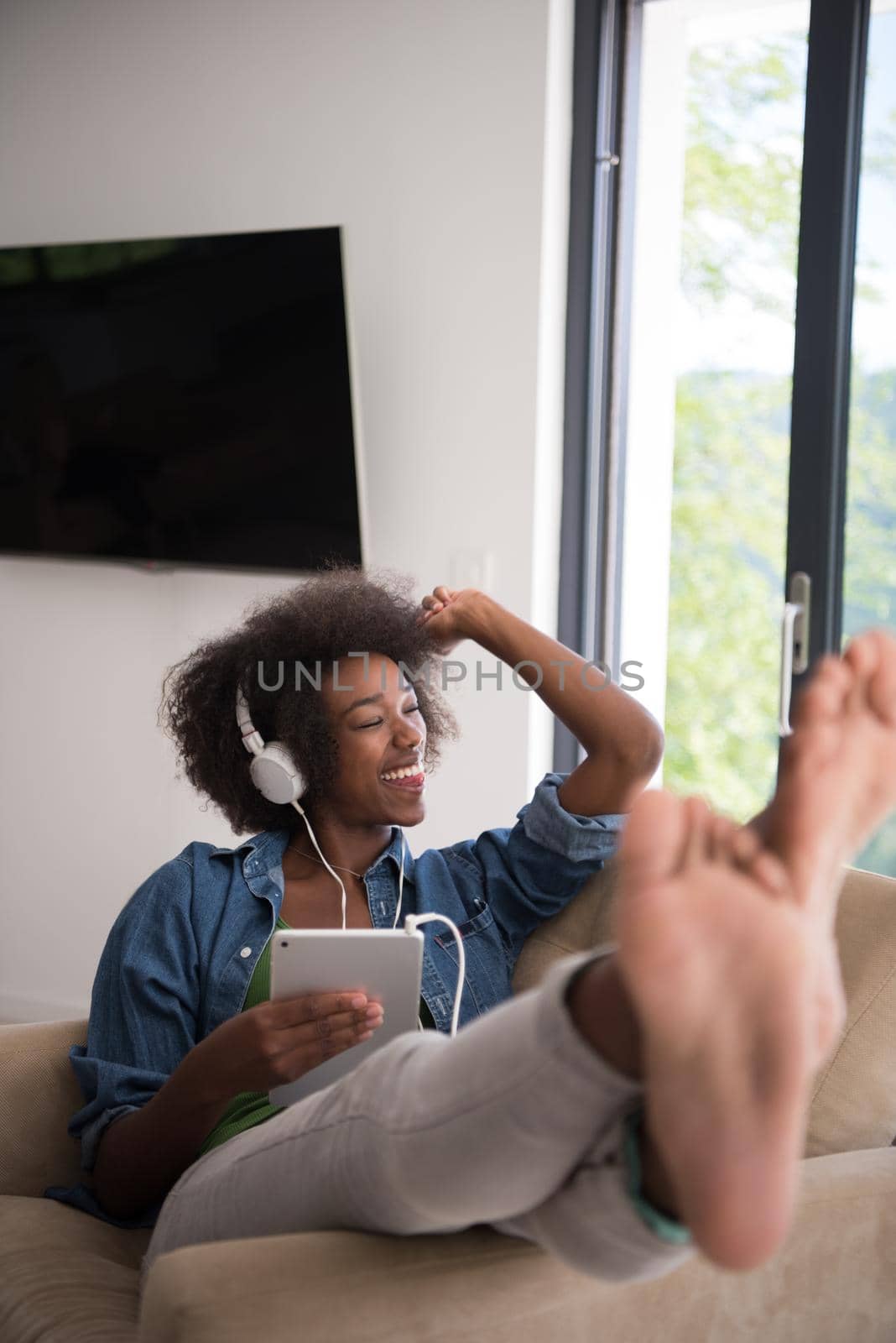 African american woman at home in chair with tablet and head phones by dotshock