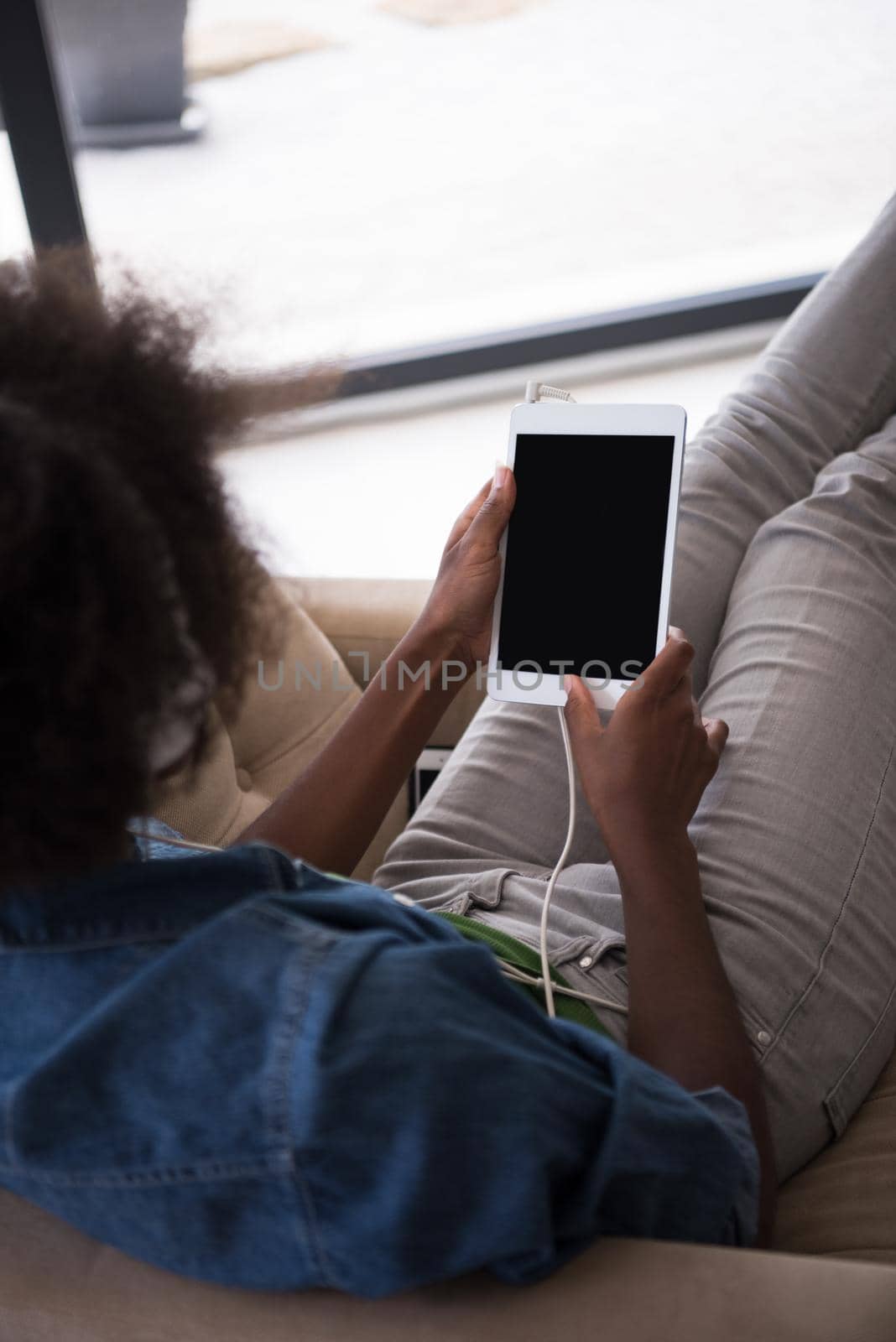 African american woman at home in chair with tablet and head phones by dotshock