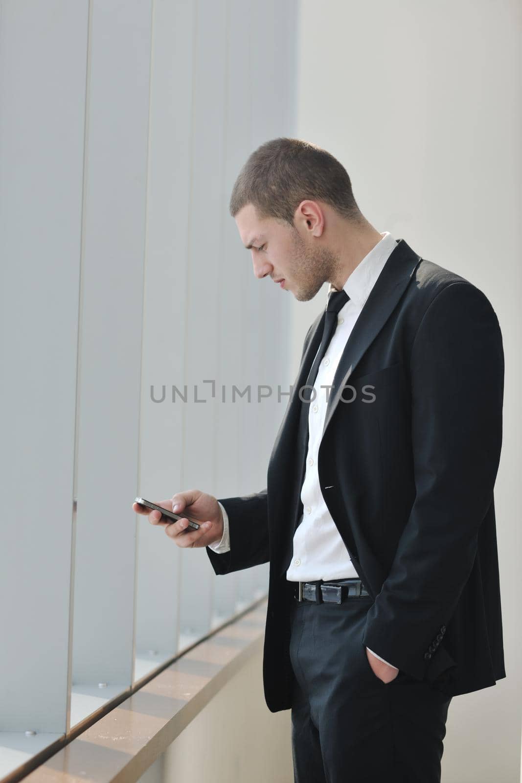 young business man talk by cellphone over bright window in big hall 