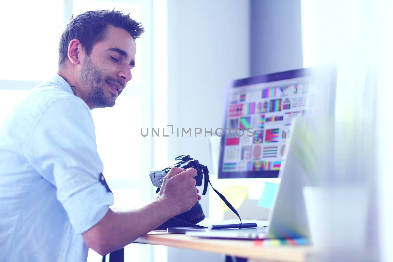 Portrait of young designer sitting at graphic studio in front of laptop and computer while working online