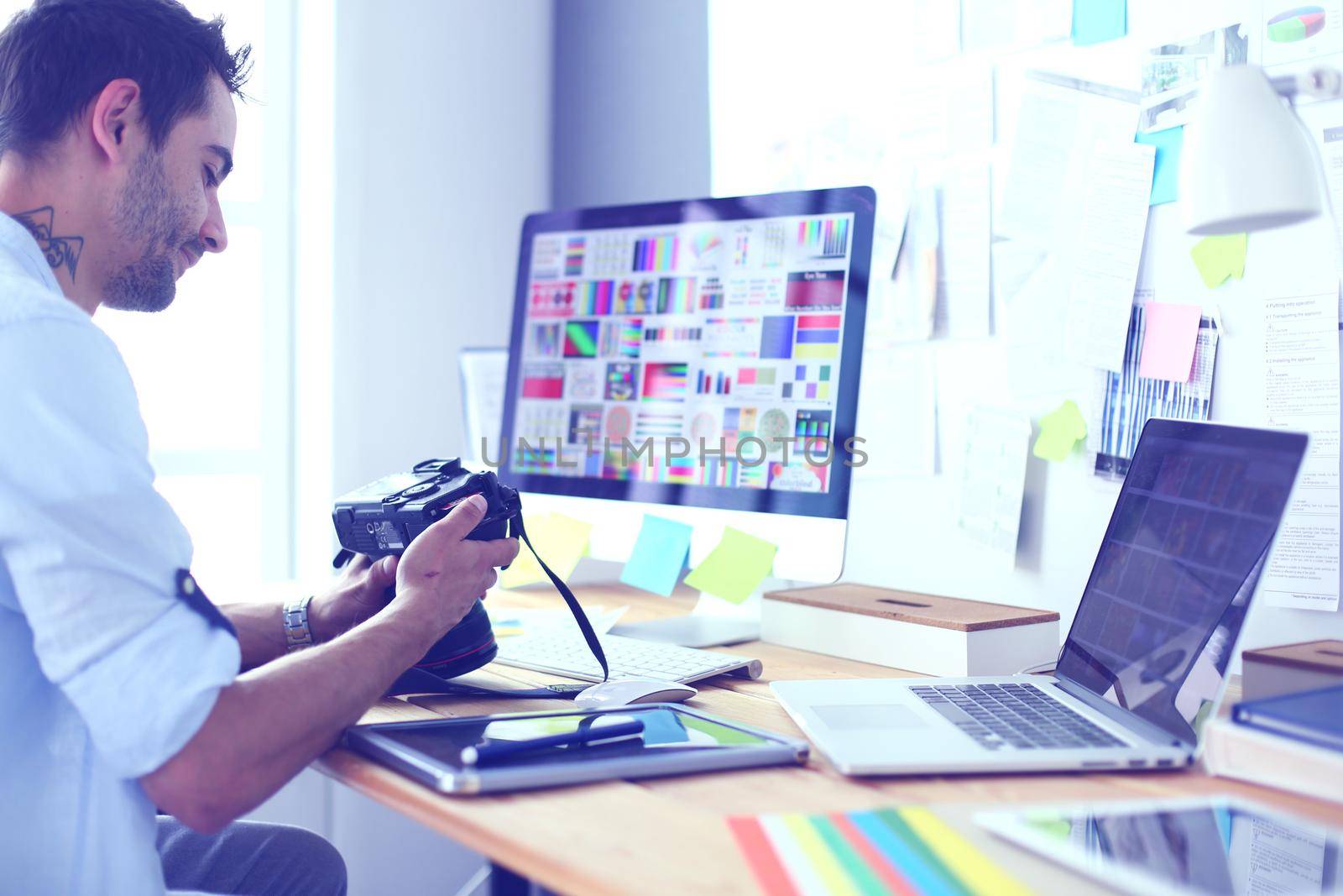 Portrait of young designer sitting at graphic studio in front of laptop and computer while working online. by lenets