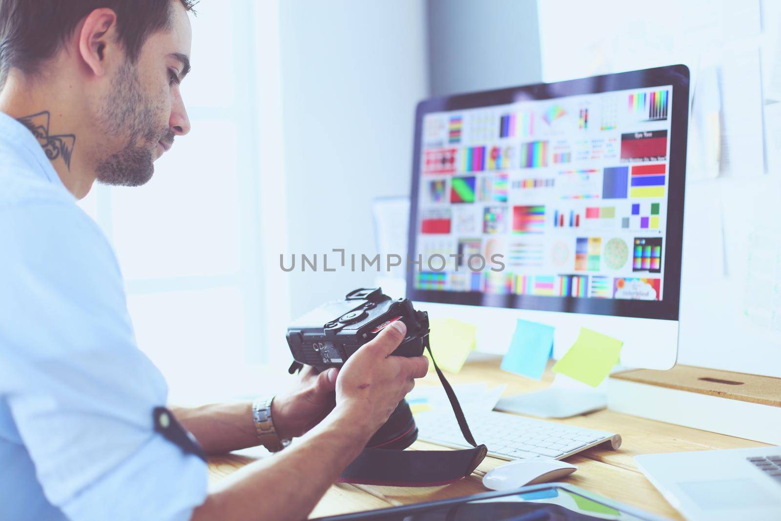 Portrait of young designer sitting at graphic studio in front of laptop and computer while working online