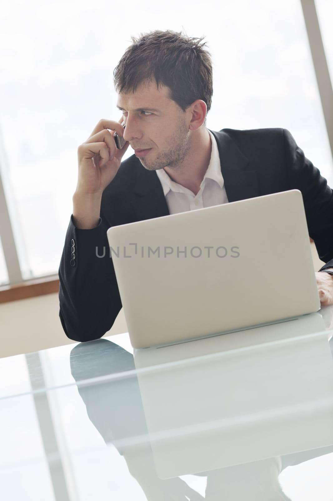 young business man talk by cellphone over bright window in big hall 