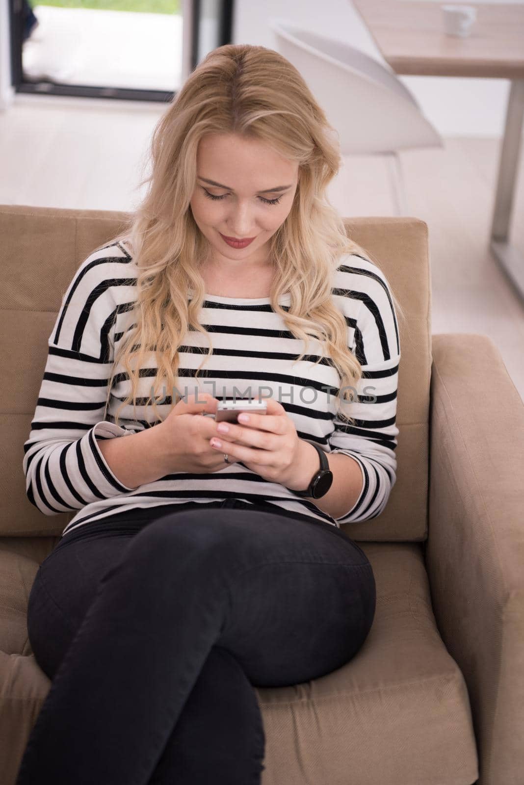 young happy woman sitting on sofa with mobile phone at luxury home