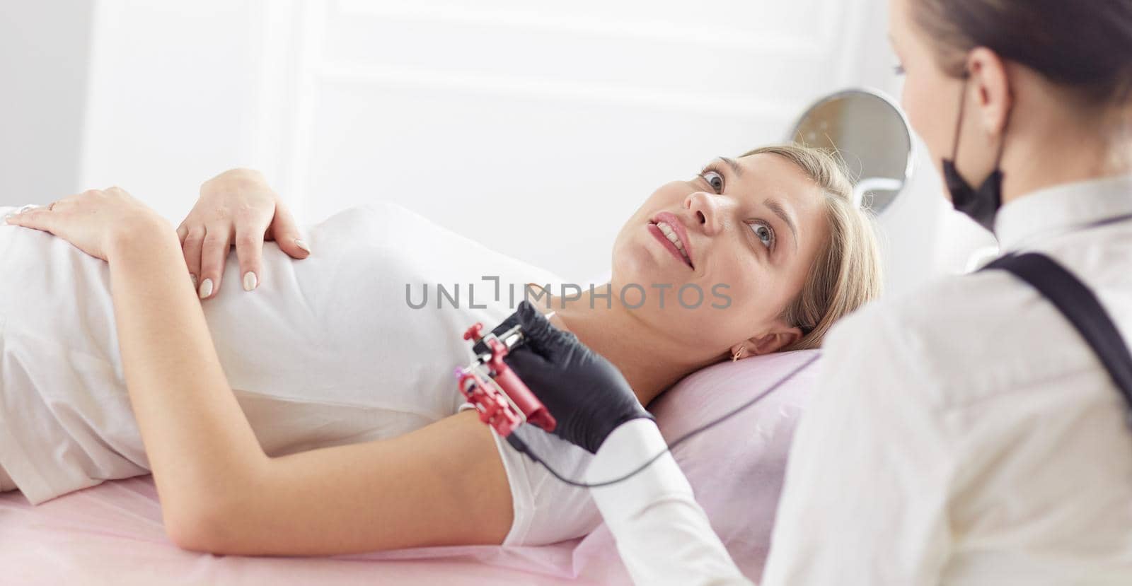 Young woman undergoing procedure of eyebrow permanent makeup in beauty salon.