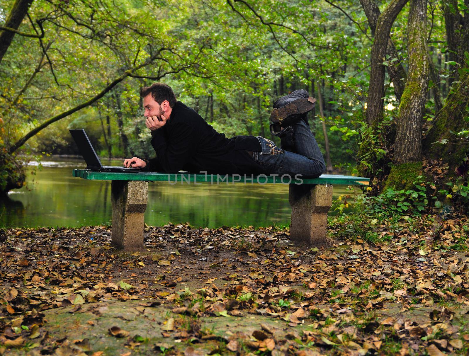 one young businessman working on laptop outdoor with green nature in backgroundone young businessman working on laptop outdoor with green nature in background