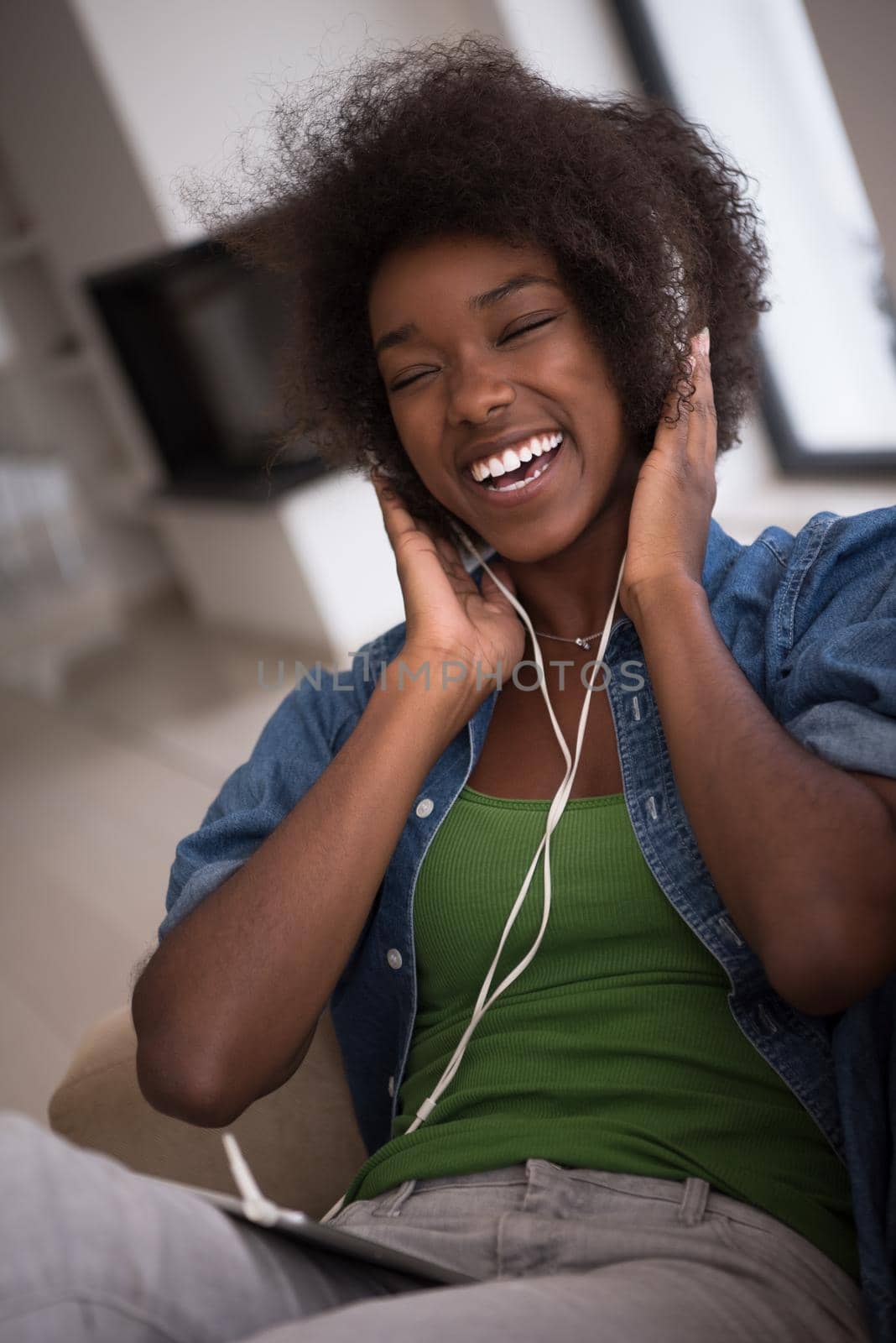 young beautiful African American woman enjoys listening to music with headphones and tablet in your armchair in her luxury home