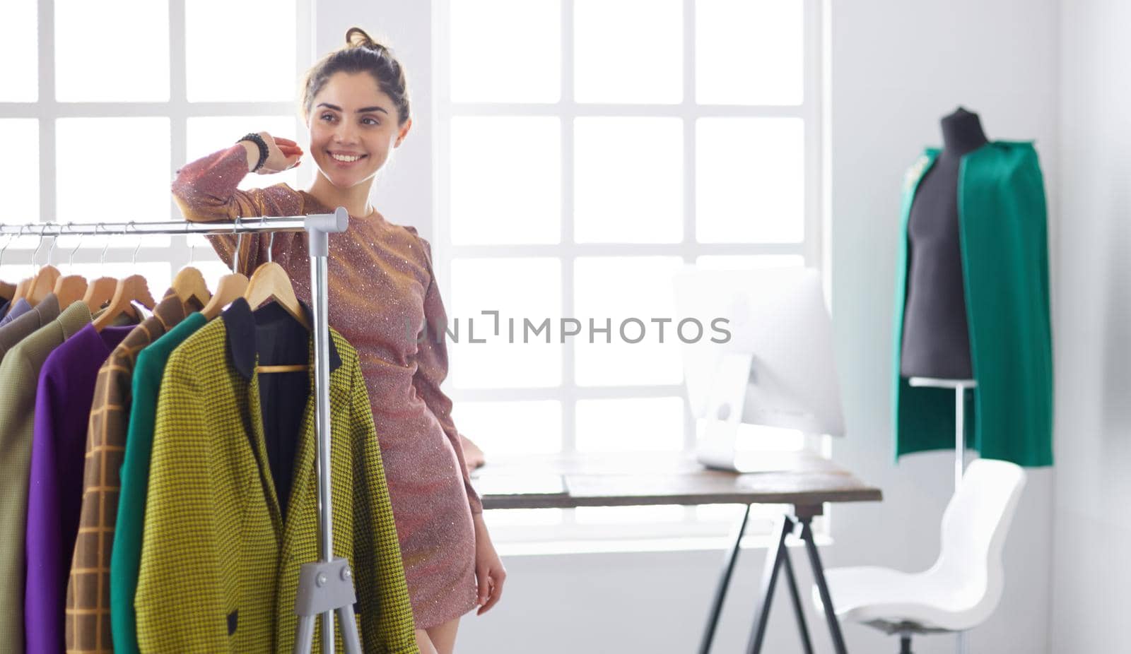 Beautiful young stylist near rack with hangers.