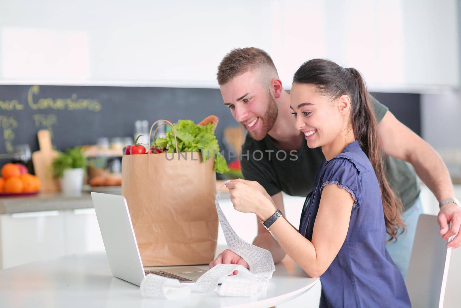 Couple paying their bills with laptop in kitchen at home.