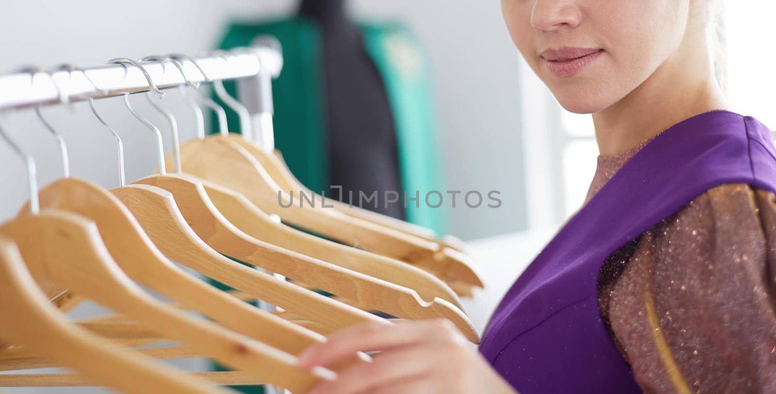 Beautiful young stylist near rack with hangers.