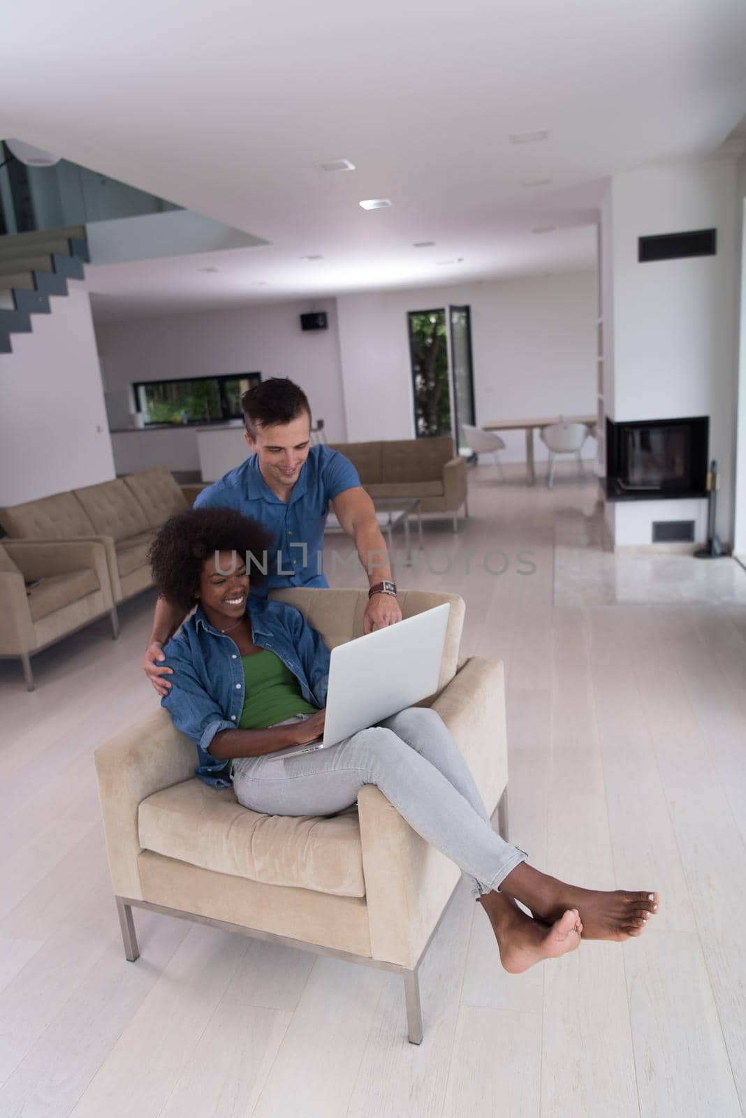 Young multiethnic couple sitting on an armchair in the luxury living room, using a laptop computer
