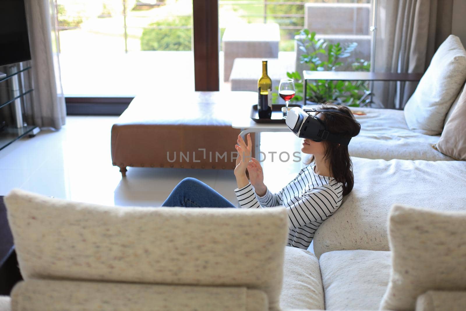 Young casual girl wearing VR headset while lounging on the floor near couch at home and looking around