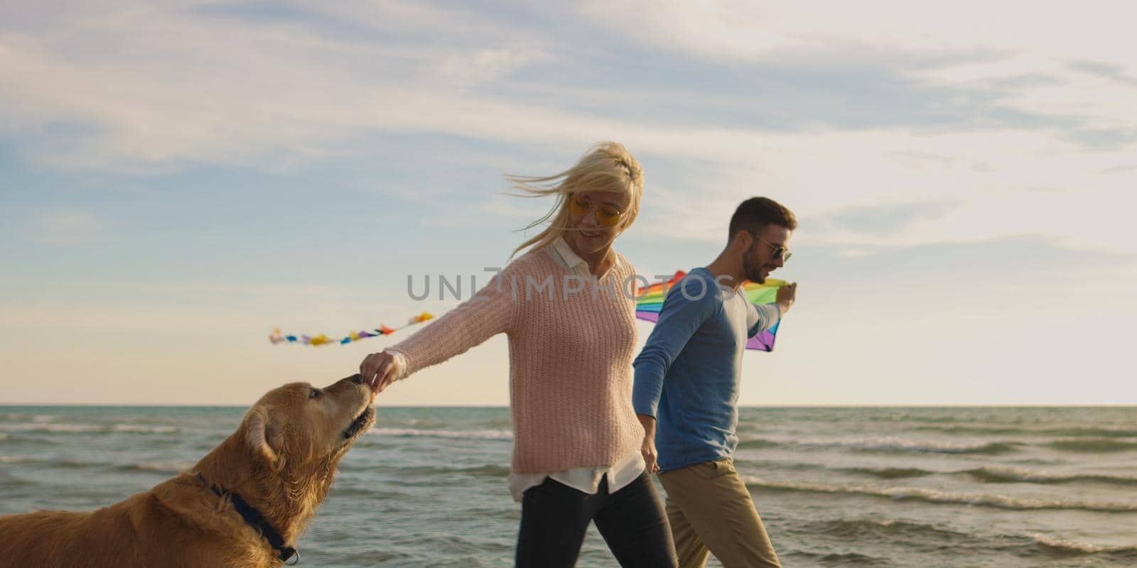 Couple Running On The Beach Holding Their Hands with dog On autmun day