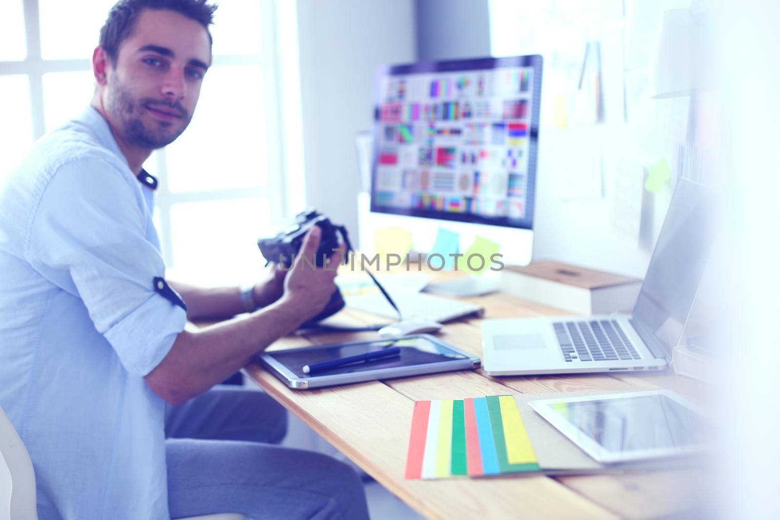 Portrait of young designer sitting at graphic studio in front of laptop and computer while working online