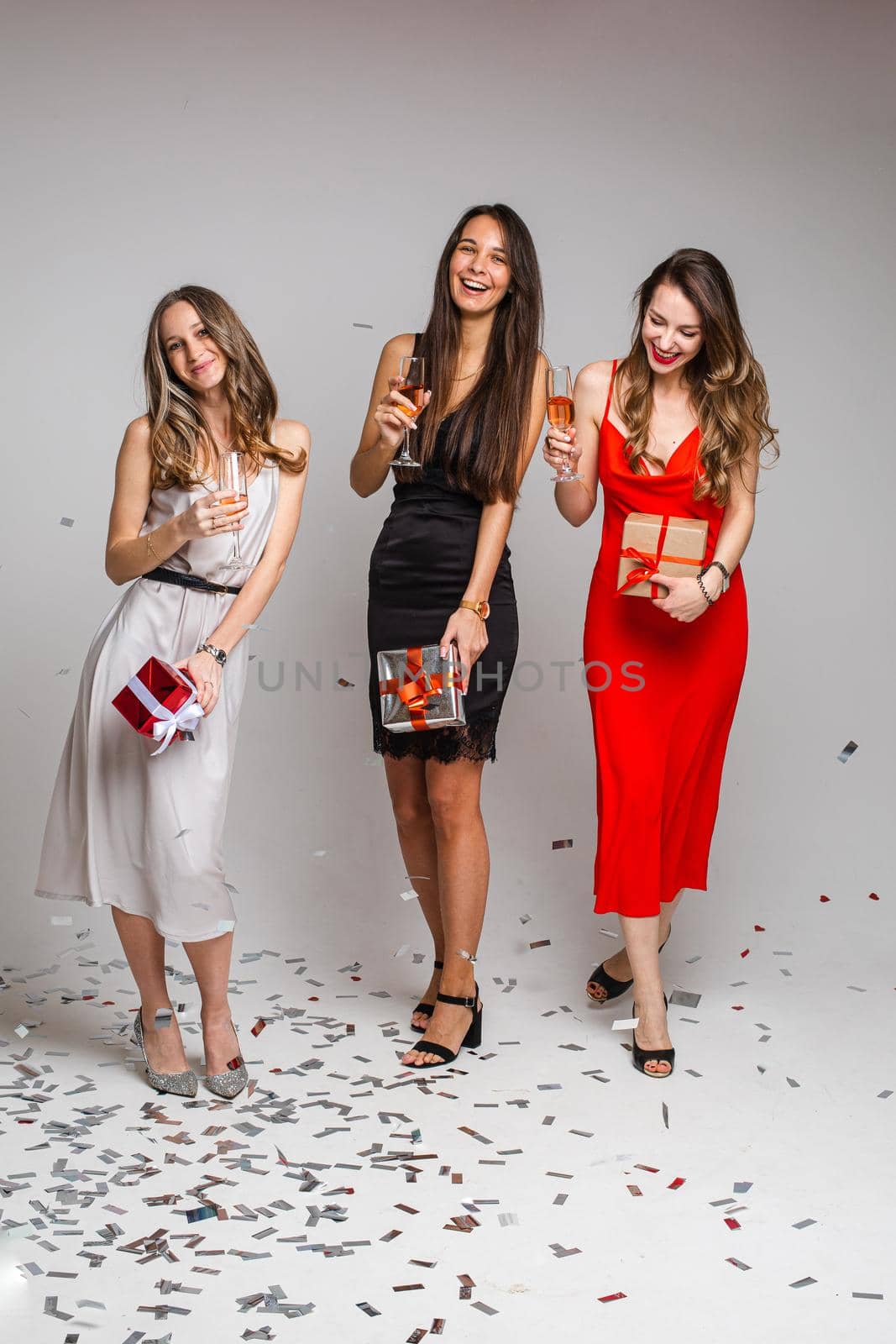 three cheerful friends in beautiful dresses celebrate new year with glasses of wine by StudioLucky