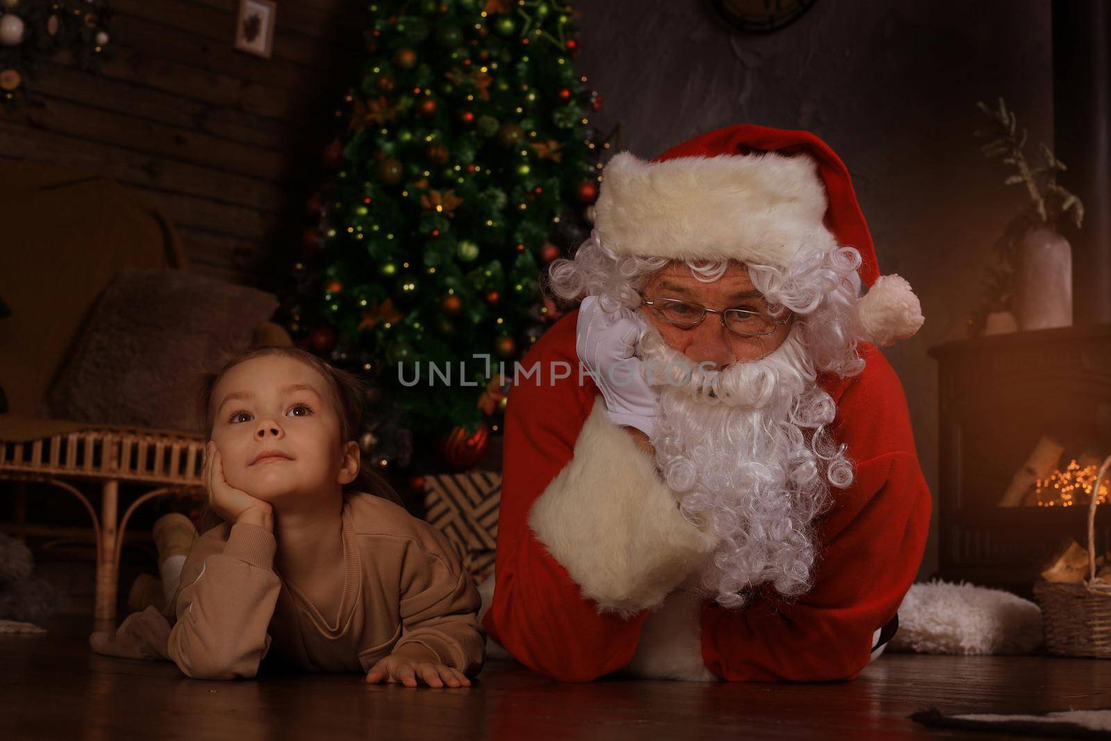 Santa Claus and child laying on floor at home. Christmas gift. Family holiday concept. by tsyhun