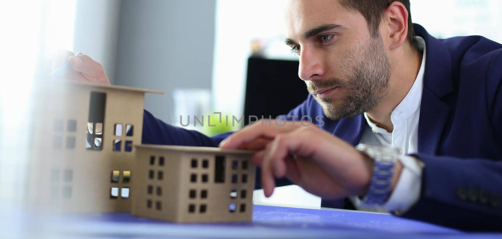 Businessman holding house miniature on hand standing in office. by lenets