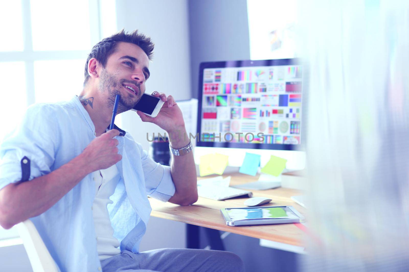 Portrait of young designer sitting at graphic studio in front of laptop and computer while working online