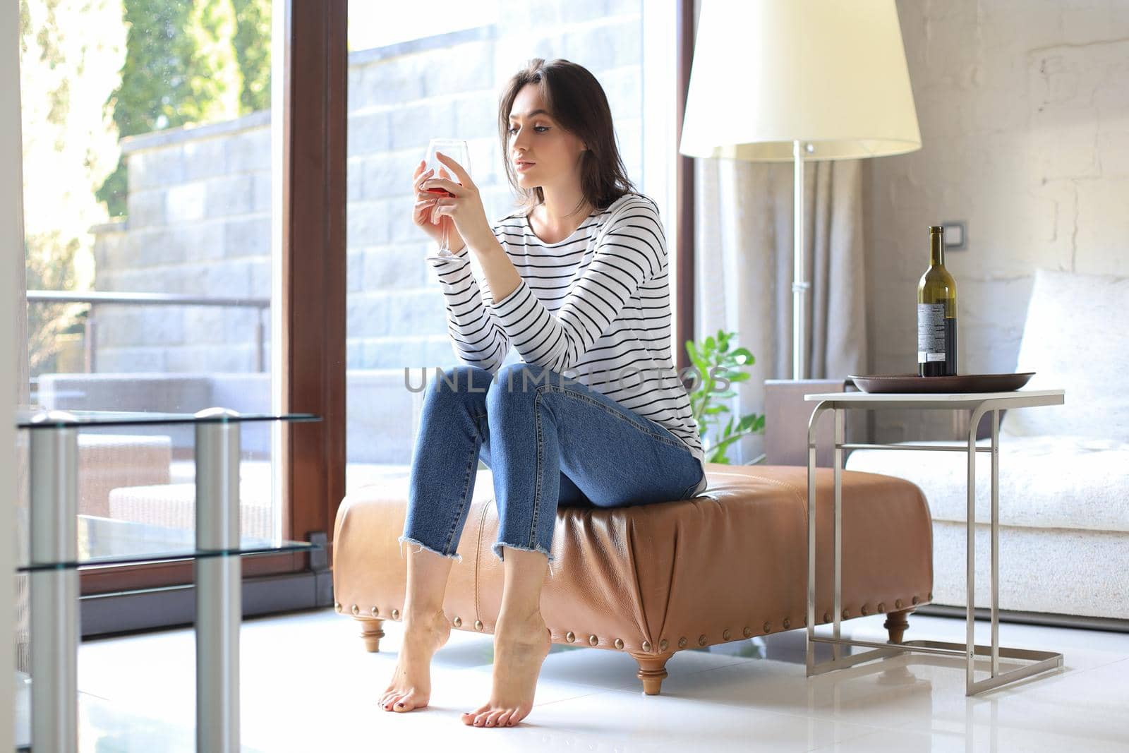 Successful young beautiful woman sitting on an armchair in the living room, drinking red wine